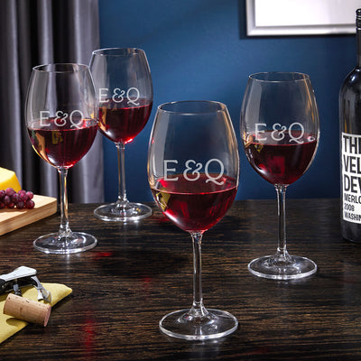 Four wine glasses with red wine and “E&Q” etched on them on a wooden table, with a wine bottle nearby.