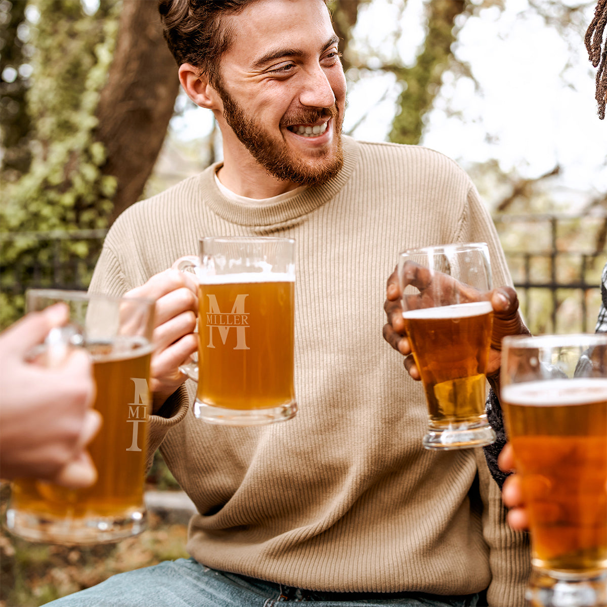 Smiling man holding a beer mug as others raise beer glasses in an outdoor setting.